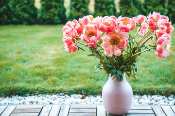 A bouquet of vibrant pink peonies with copy-space. These flowers are housed in a pink, ribbed vase, which is placed on a wooden floor