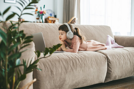 A cute little girl is absorbed in her laptop, wearing headphones to immerse herself in the digital world. Concept: technology-infused relaxation, online education, technological entertainment
