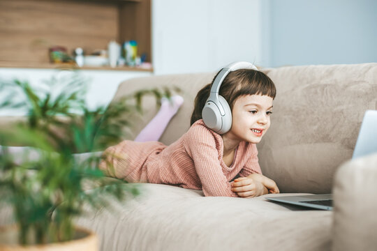 A delightful little girl, aged 5-6 years old, wearing headphones while captivated by the laptop screen. Concept: technology-infused relaxation, online education, computer entertainment