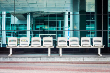 Two 4-seat bus waiting benchs at a modern bus stop station. The seats are white and are made of metal.