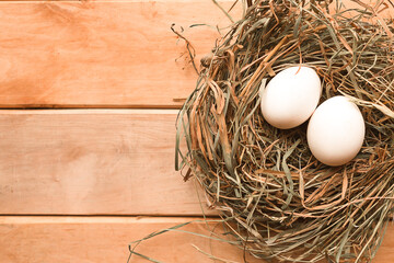 Eggs in hay nest on wooden background. Easter concept