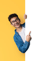 Excited young man wear eye glasses, braces, stand behind, peep from blank empty banner mockup sign board signboard, advertise show area for sales slogan text, isolate yellow background. Dental care ad
