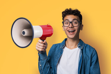 Funny very happy brunette young man wear glasses dent dental tooth braces brackets advertise use mega phone megaphone loudspeaker bullhorn open mouth, isolated yellow background. Sales ad concept