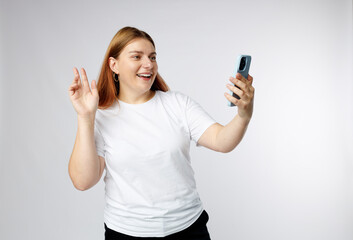 Laughing young woman taking selfie on on white background, studio portrait. Cute beautiful woman using mobile phone. 30s girl recording self video, talking on online call