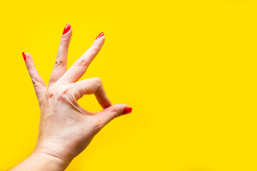 Woman's hand shows the OK gesture over bright yellow background. Minimal concept. Copy space for...