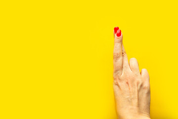 woman's hand crosses fingers over bright yellow background, copy space for the text