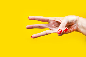 woman's hand shows three gesture over bright yellow background