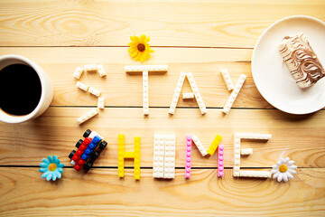 Phrase Stay at Home from toy constructor and coffee cup on wooden background. Quarantine concept