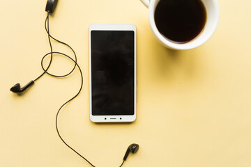 Mobile phone with black mockup screen and coffee cup on yellow background. Minimal concept