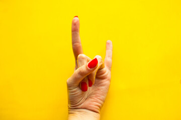 Woman's hand shows a gesture Rock over bright yellow background.