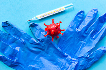 Medical gloves, red model virus and thermometer on blue background. Covid-19 concept