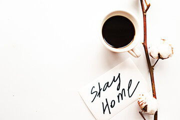 Cotton branch, coffee and card with text Stay Home on white background. Quarantine concept. Copy...