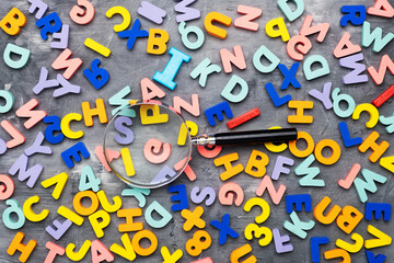 Colorful alphabet letters and magnifying glass on gray background and texture, top view