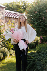 Schoolgirl with a bouquet of flowers at the start of the school year in uniform .Teen girl holds a bouquet of flowers and goes to school.white embroidered shirt and black pants. Embroidered Shirt. - obrazy, fototapety, plakaty