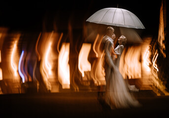 Valmiera, Latvia - August 10, 2023 - Bride and groom under an umbrella with motion-blurred lights...