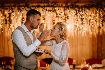 Valmiera, Latvia - August 10, 2023 - Bride and groom feeding each other cake with twinkling lights...