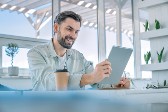 Smiling man working on his digital tablet at a coffee shop. Cheerful young coworker freelancer ceo manager tutor typing, scrolling social media, doing shopping online in office - Powered by Adobe
