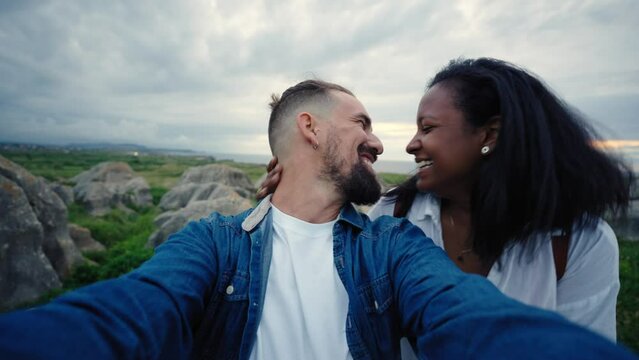 Happy multiracial couple making a selfie video outdoors in the nature enjoying their holidays, looking at the camera with big smiles feeling the freedom on honeymoon.