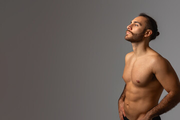 Bare-Chested Man Standing Before Gray Background, Copy Space - obrazy, fototapety, plakaty