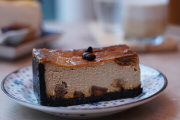 A piece of espresso macadamia cheese cake topped with coffee beans on the plate with blur of blueberry crepe cake and dirty latte coffee.