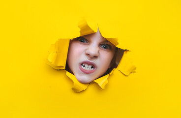 A little ukrainian girl looks through a torn hole in yellow paper. The concept of anger, fear, fright and shock from what he saw. Unexpected aggression and stress. Copy space.