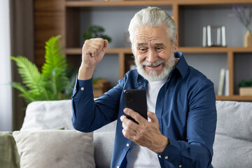 Senior man celebrating good news on smartphone at home