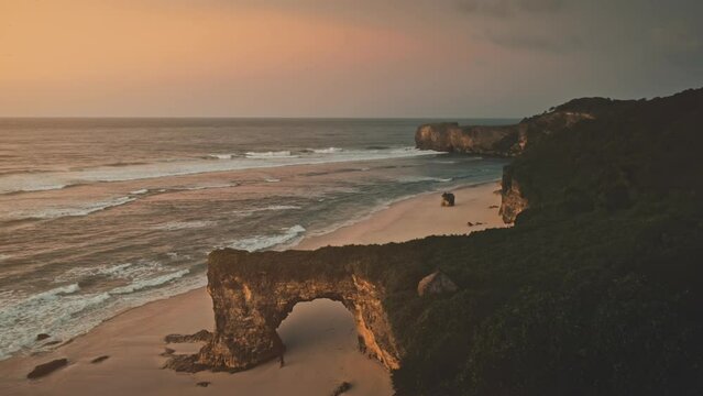 Slow motion of wavy sea at rock wall with giant hole aerial view. Nobody nature scape of Sumba island, Indonesia. Sun set light of cinematic summer scenery. Natural beauty of ocean waves at sand beach