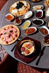A sumptuous Turkish lunch, the menu of which presents a symphony of flavors. The menu includes bread, cheeses, sliced fresh fruits, pickled vegetables, snacks, hummus. Turkish tea in bowls.