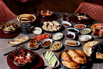 A sumptuous Turkish lunch, the menu of which presents a symphony of flavors. The menu includes bread, cheeses, sliced fresh fruits, pickled vegetables, snacks, hummus. Turkish tea in bowls.