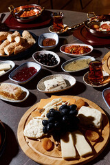 A sumptuous Turkish lunch, the menu of which presents a symphony of flavors. The menu includes bread, cheeses, sliced fresh fruits, pickled vegetables, snacks, hummus. Turkish tea in bowls.