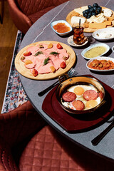 A sumptuous Turkish lunch, the menu of which presents a symphony of flavors. The menu includes bread, cheeses, sliced fresh fruits, pickled vegetables, snacks, hummus. Turkish tea in bowls.