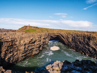 Tourist enjoy stunning Bridges of Ross in county Clare, Ireland. Rock formation arched over ocean...