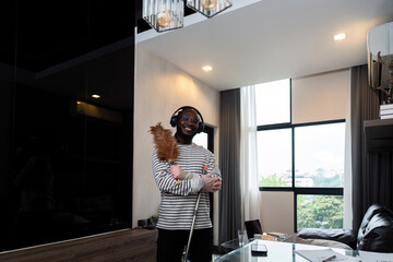 Young African American man for cleaning apartment, holding mop and other cleaning tools. Cheerful...