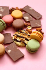 Pastel macarons, almond chocolate, peanut butter cookies and various nuts on bright pink background. Selective focus.