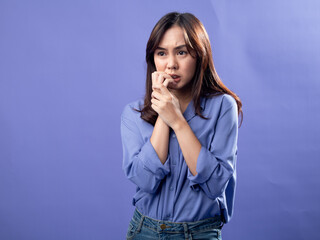 A young Asian woman in a light blue button-up shirt and jeans stands against a solid lavender...