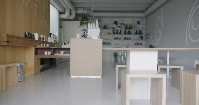 This image features a modern coffee shop with a minimalist design, showcasing wooden furniture, a well-organized counter, and decorative plants. The space is clean and inviting