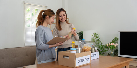 Fototapeta na wymiar Donation and two woman volunteer asian of happy packing food in box at home. Charity