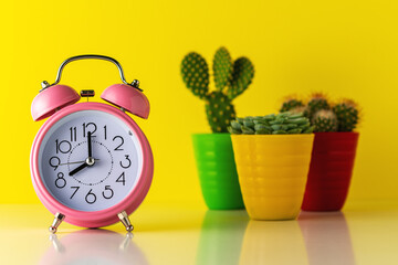 Pink alarm clock with cactus in pot on wooden desk. Minimal time concept.