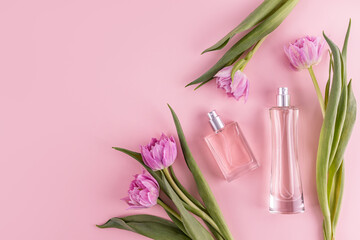 Two stylish glass bottles with perfume on a pink background among spring flowers. A copy space. Top view. Perfume and beauty concept.