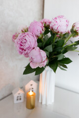 tea in a white cup, pink peonies, flowers and candles of golden color on a white background.Laptop, beautiful pink peony bouquet and notebook on white table background. minimalist home workspace. 
