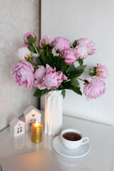tea in a white cup, pink peonies, flowers and candles of golden color on a white background.Laptop, beautiful pink peony bouquet and notebook on white table background. minimalist home workspace. 