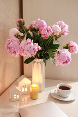Obraz na płótnie Canvas tea in a white cup, pink peonies, flowers and candles of golden color on a white background.Laptop, beautiful pink peony bouquet and notebook on white table background. minimalist home workspace. 