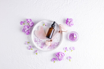 Cosmetic dropper bottle with natural organic product for care and massage on ceramic plate with roller for massage. lilac delicate flowers.