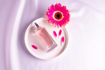 An elegant bottle with a natural floral fragrance on a ceramic plate with a pink gerbera flower....