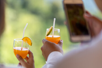 selective focus glasses of freshly squeezed orange juice in the hands of men and women clinking glasses of fresh tangerine juice Orange slices inserted into a glass
