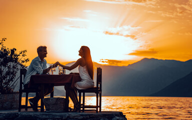 Fototapeta na wymiar Couple in love drinking champagne wine on romantic dinner at sunset on the beach