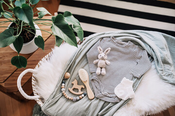Still life background of cute baby products - changing basket with baby bodysuit, newborn clothes, knitted rabbit and wooden toy. Minimalist style photography of baby shower, pregnancy announcement. - 793939875