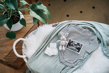 Baby changing basket with ultrasound image, baby bodysuit, knitted rabbit toy. Still life of child products. Newborn background. Minimalist style photography of baby shower, pregnancy announcement.