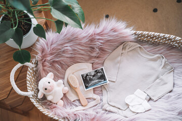 Baby changing basket with ultrasound image, baby bodysuit, soft and wooden toys. Still life of child products. Newborn background. Minimalist style photography of baby shower, pregnancy announcement. - 793940009