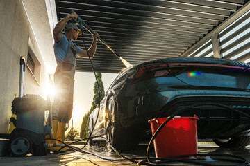 Man Pressure Washing His Modern Car Inside a Carport